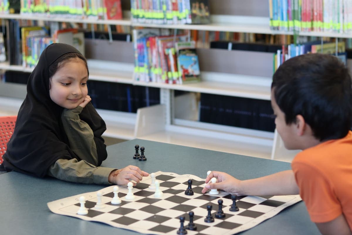 Two students playing chess together at the library