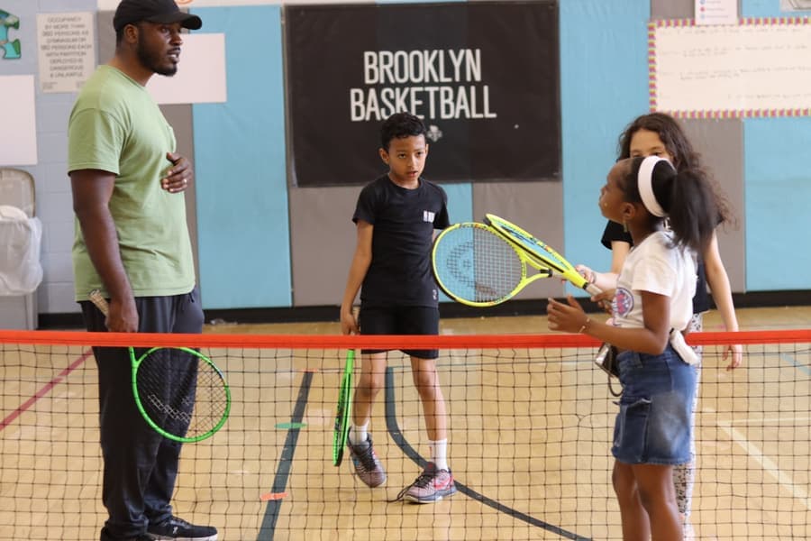 A coach and young players rallying over a mini tennis net in the gym