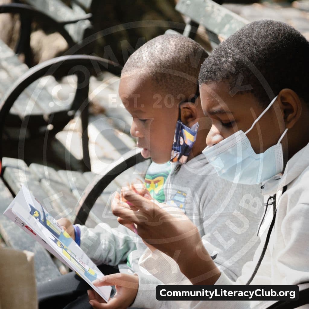Two boys reading a picture book together on a park bench