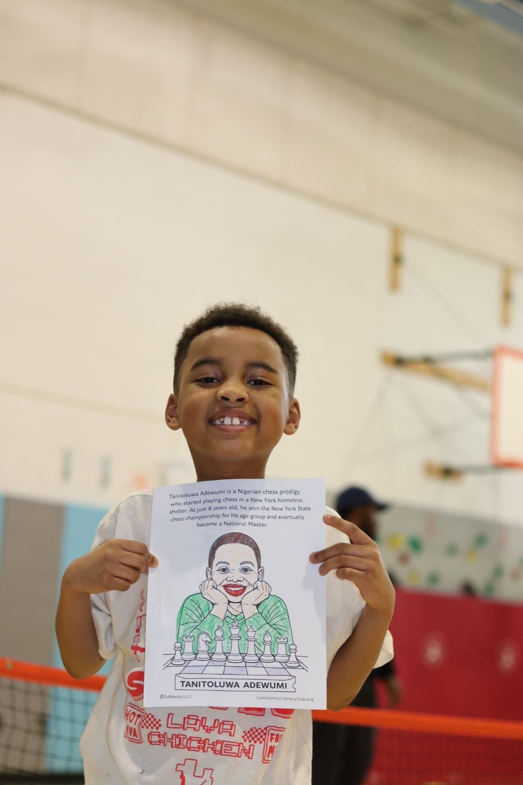 A smiling student holding up a CLC workshop handout in the gym