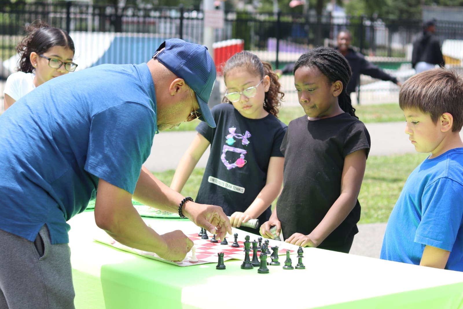 A volunteer teaching a group of kids chess at an outdoor community event