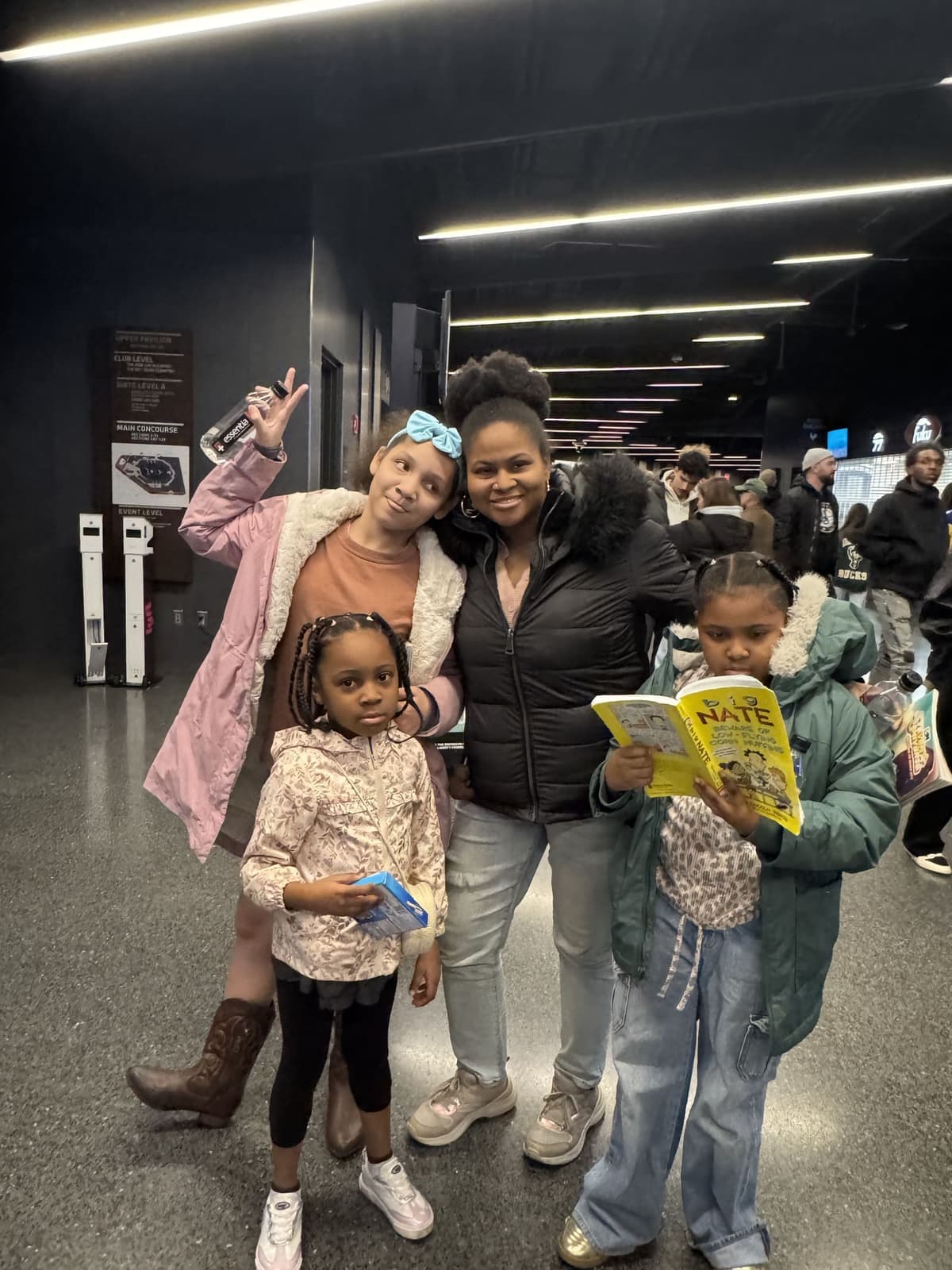 A mentor and three girls at an arena outing, one reading a Big Nate book