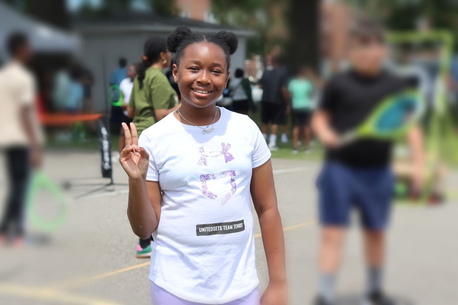A girl flashing a peace sign at an outdoor CLC tennis clinic