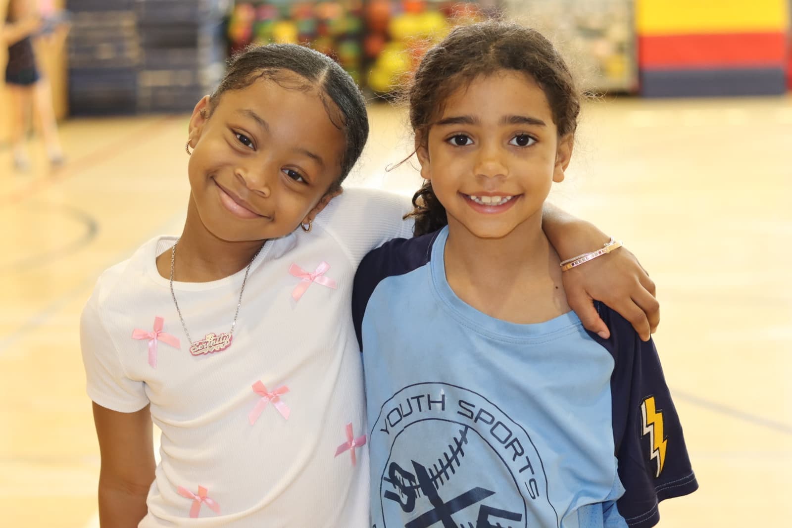 Two girls smiling arm in arm in the gym