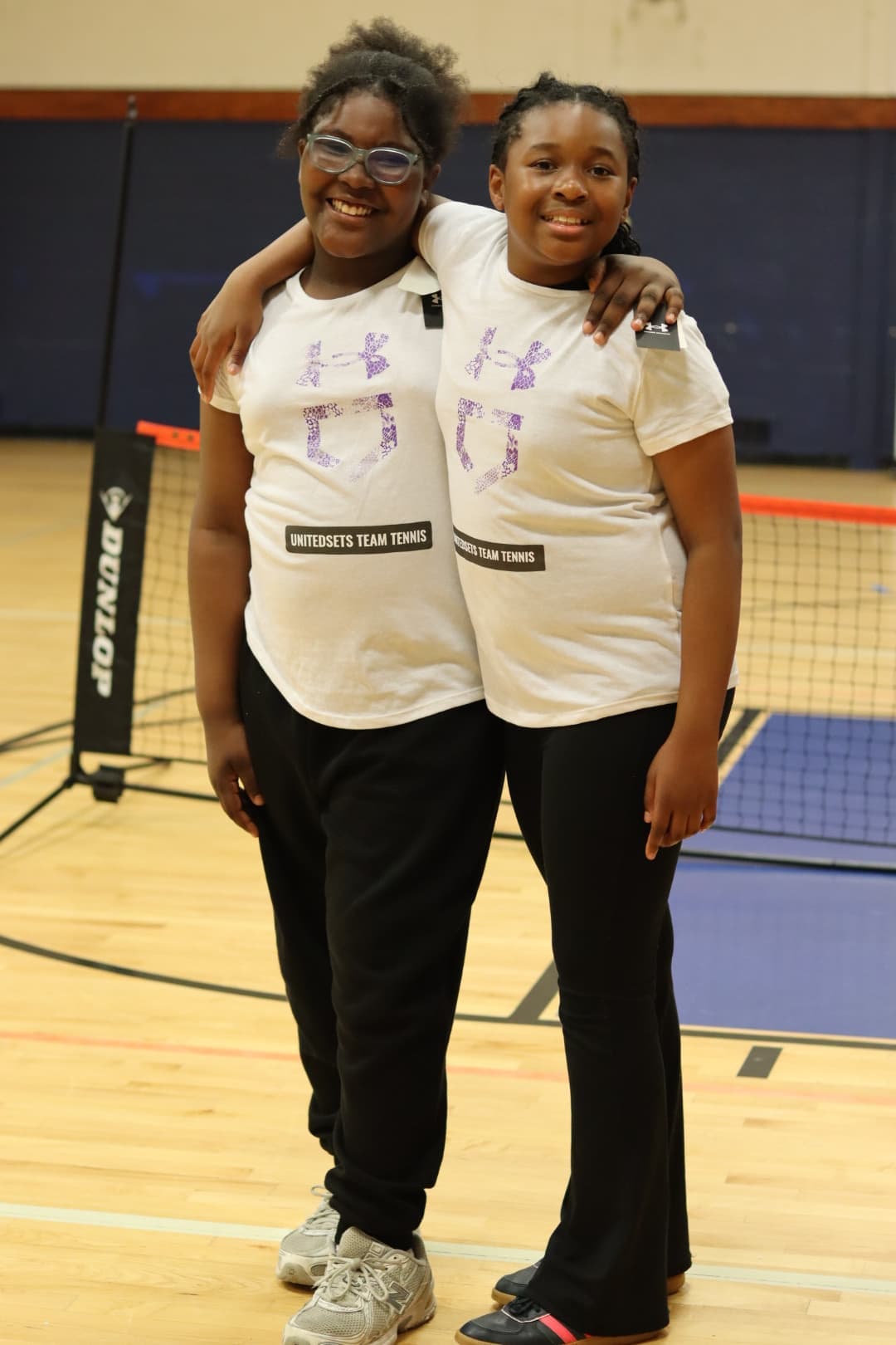Two UnitedSets teammates arm in arm beside the net in the gym