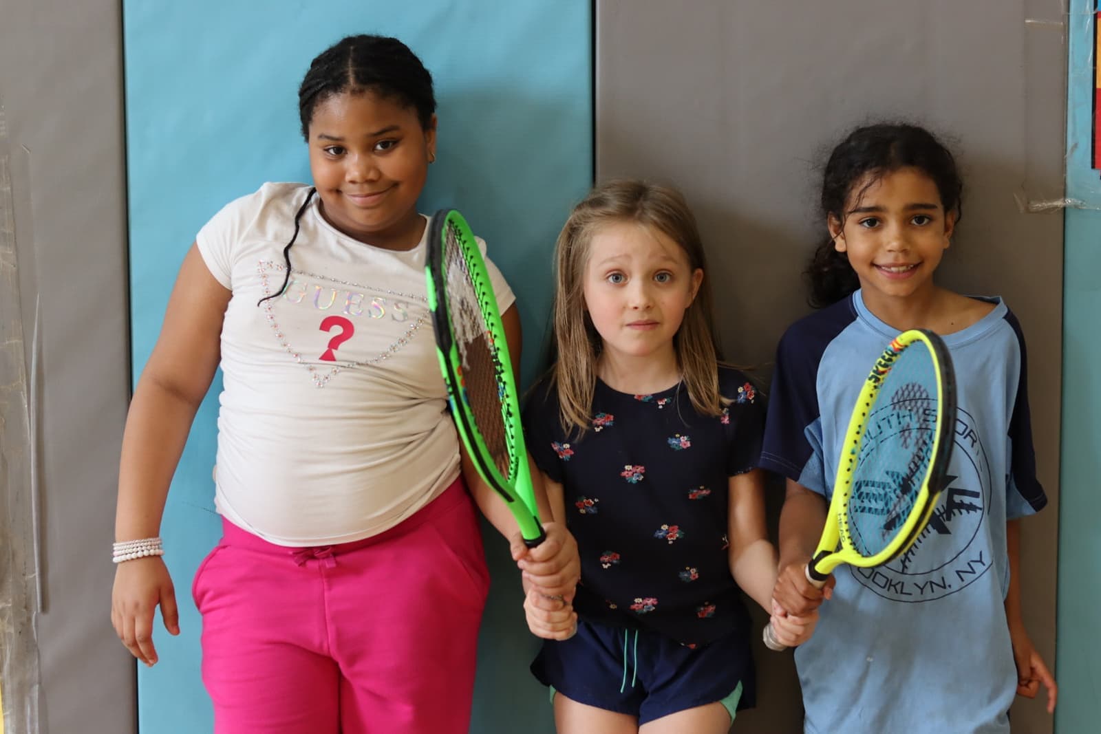 Three girls smiling with their tennis rackets in the gym