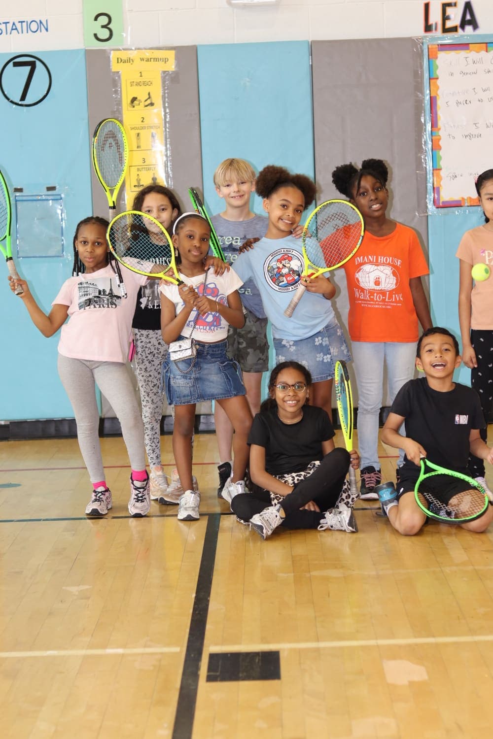 A joyful group of young players holding up their tennis rackets in the gym