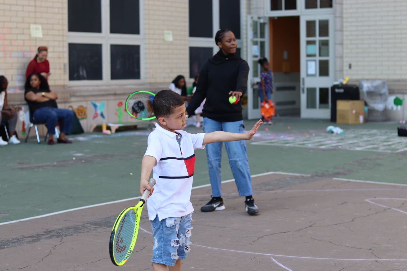 A volunteer coach tossing a ball to a young player at an outdoor clinic